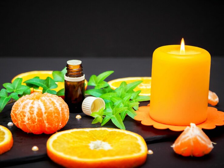 Orangenschalen, Duftöl und eine angezündete Kerze in Orange